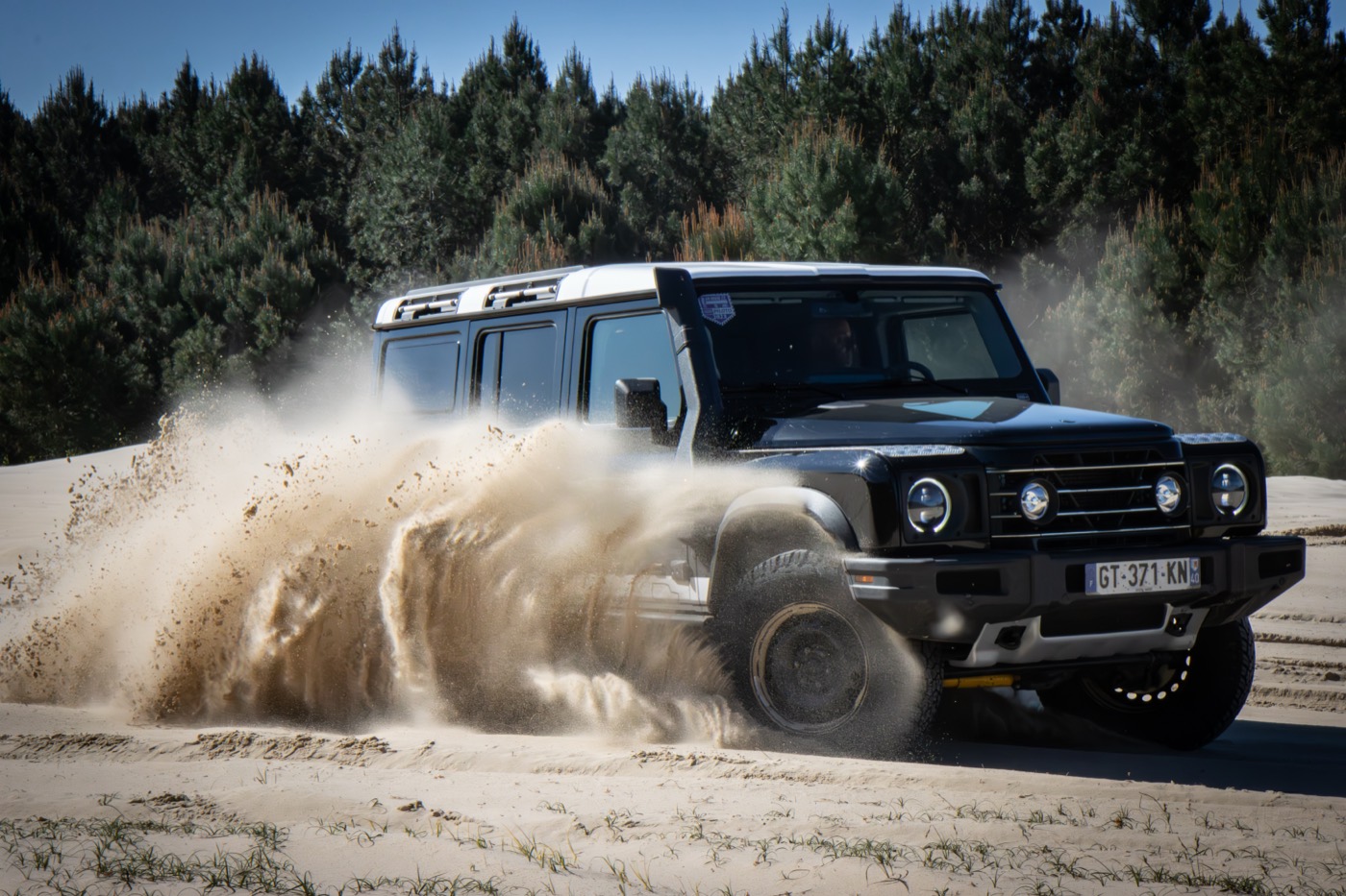 Black INEOS Grenadier throwing up sand on a fast track